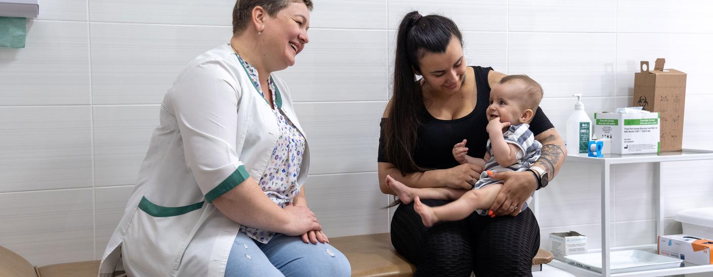 Une infirmière souriante et une mère tenant un bébé de huit mois dans un centre de santé à Kiev, en Ukraine, se préparant à la vaccination.