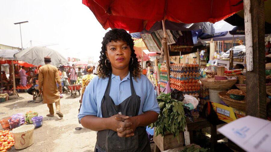 Une vendeuse de marché se tient à son étal au Nigéria, au milieu d'une activité commerciale, illustrant l'impact de la hausse des prix des denrées alimentaires et de la faim.