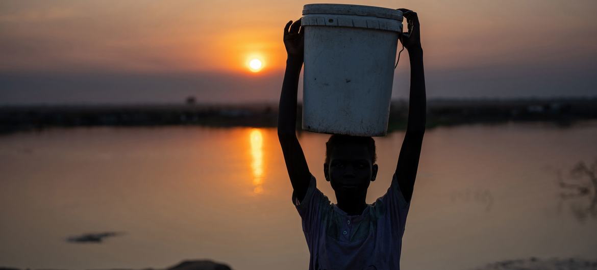 दक्षिण सूडान में, एक लड़की, दूर स्थान से पानी भरकर, विस्थापितों के लिए बनाए गए शिविर में अपने निवास के लिए ले जाते हुए.