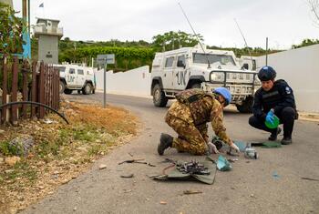 A UNIFIL forensic investigator and an Italian Carabinier examine drone remnants on the ground near a road in Naqoura.