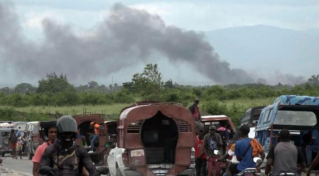 Des habitants fuient Cité Soleil vers Drouillard, à Port-au-Prince, en Haïti, tandis qu'une épaisse fumée s'élève en arrière-plan, conséquence d'affrontements entre groupes armés.