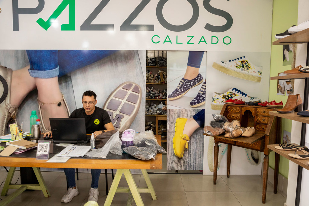 Un hombre trabaja con un ordenador portátil en una zapatería de Ecuador, que da empleo a refugiados y migrantes.