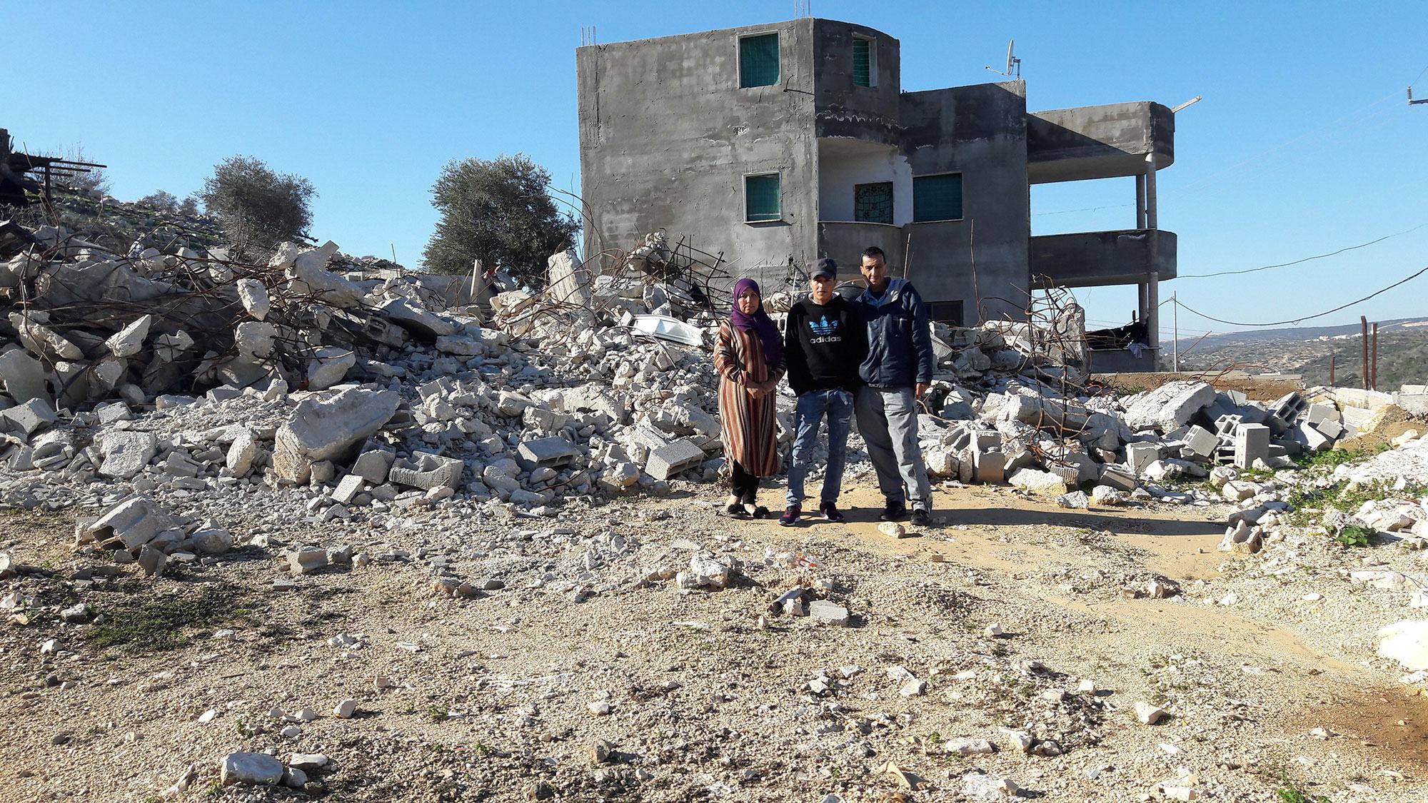 عائلة فلسطينية تقف بجوار كومة من الأنقاض من منزل مدمر في جنين، الضفة الغربية.