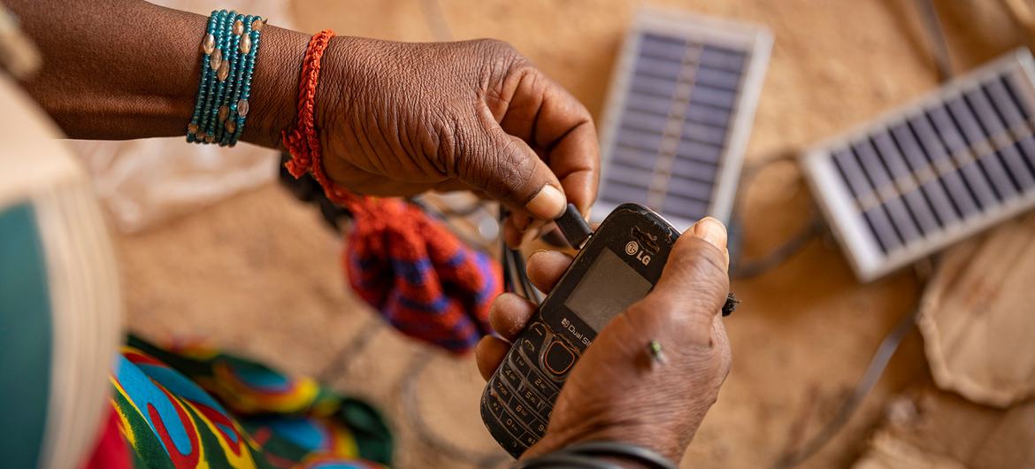 Burkina Faso'daki yerinden edilmiş kişiler kampında bir kadın cep telefonunu şarj etmek için güneş enerjisi kullanıyor.
