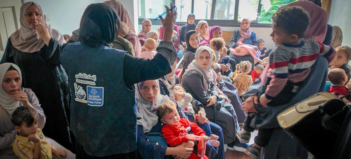 يقوم أحد العاملين في UNICEF بإعطاء حقنة لطفل صغير خلال فحص صحي في مركز للتغذية في غزة. وتنتظر مجموعة من الأمهات والأطفال في الغرفة.