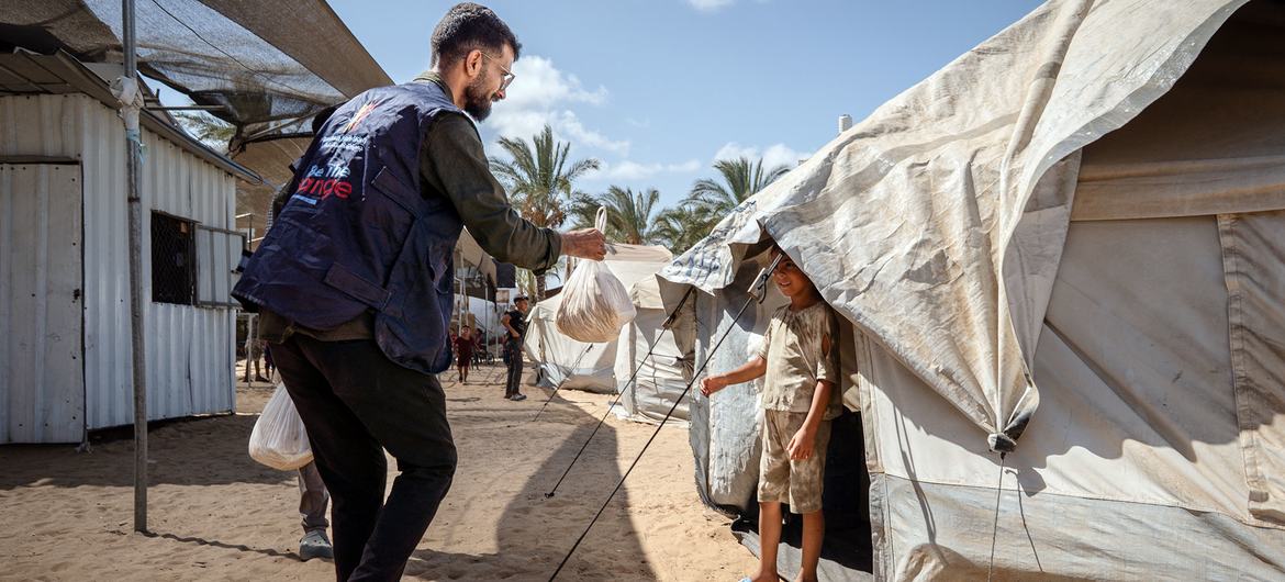 Сотрудник WFP передает пакет с хлебом мальчику в палатке в лагере беженцев в Газе.