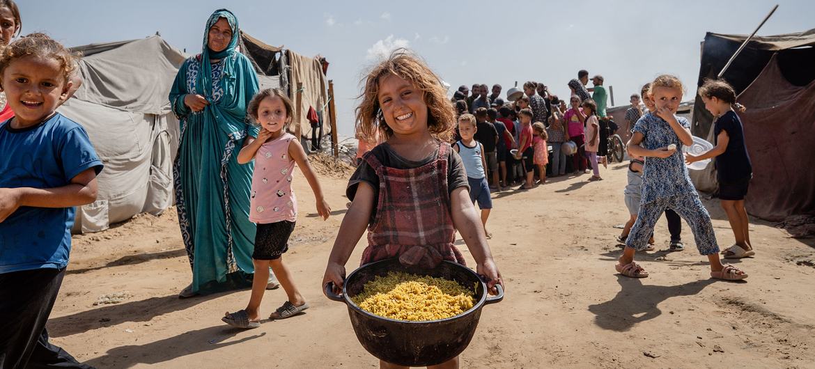 A young girl carries a pot of cooked food in Al-Mawasi, Gaza. 