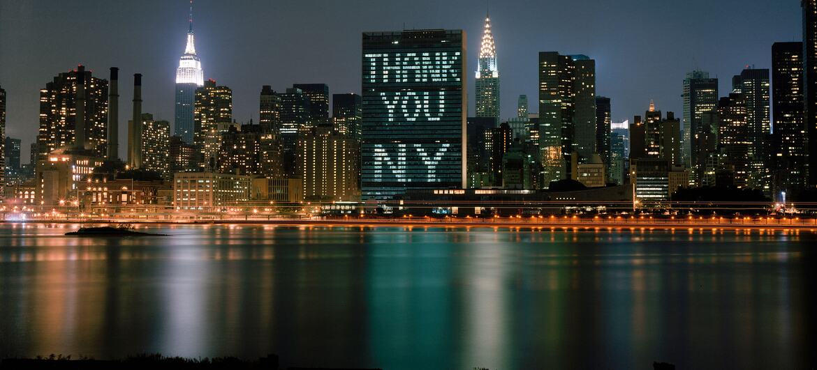 Здание Секретариата Организации Объединенных Наций освещалось словами "Благодарю Нью-Йорк" на горизонте Нью-Йорка ночью, с точки зрения Ист-Ривера.