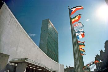 Une vue du siège des Nations Unies à New York, avec le bâtiment de l'Assemblée générale et la tour du Secrétariat, avec des drapeaux de 148 États membres en train de voler dans une rangée de plus de 500 pieds de long.