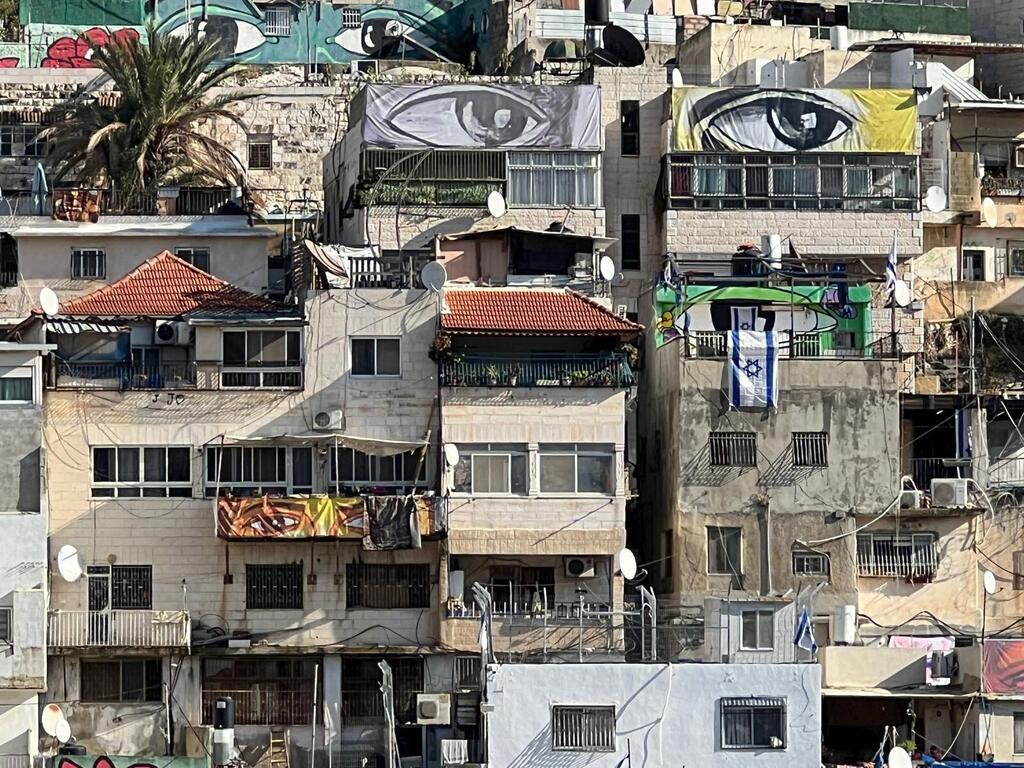 Vue aérienne de bâtiments densément emballés à Silwan, en Cisjordanie, avec de grandes peintures murales et des drapeaux israéliens visibles, mettant en évidence le paysage politique et social complexe du quartier.