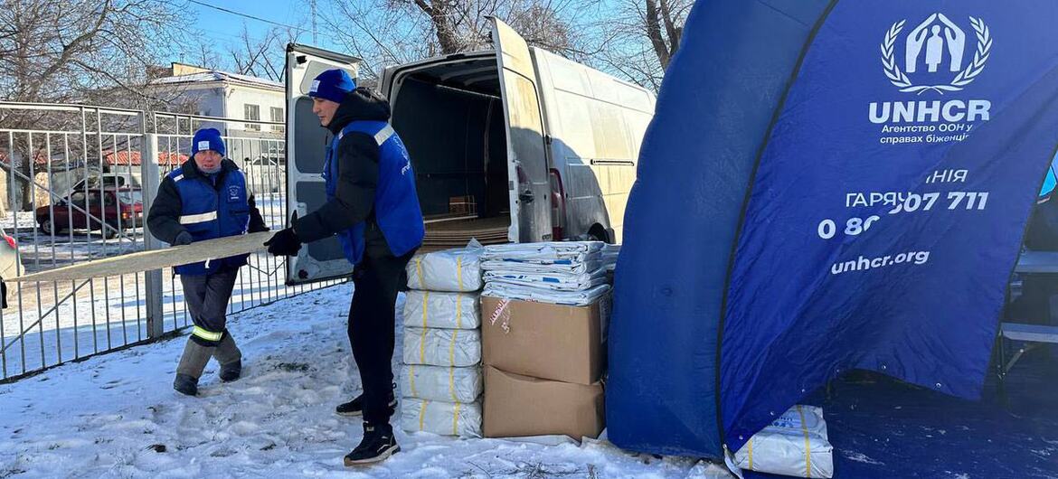 یوکرین کے برفباری شہر کریوی ریہ میں یوکرین کے دو ایچ این سی آر کے عملے نے ایک وین سے پناہ گاہ کا سامان اتار لیا۔ قریب ہی ایک نیلے رنگ کا ایچ این سی آر کا خیمہ نظر آتا ہے، جو بے گھر رہائشیوں کو تحفظ فراہم کرتا ہے۔