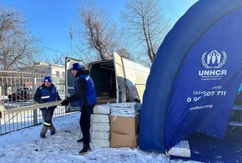 یوکرین کے برفباری شہر کریوی ریہ میں یوکرین کے دو ایچ این سی آر کے عملے نے ایک وین سے پناہ گاہ کا سامان اتار لیا۔ قریب ہی ایک نیلے رنگ کا ایچ این سی آر کا خیمہ نظر آتا ہے، جو بے گھر رہائشیوں کو تحفظ فراہم کرتا ہے۔