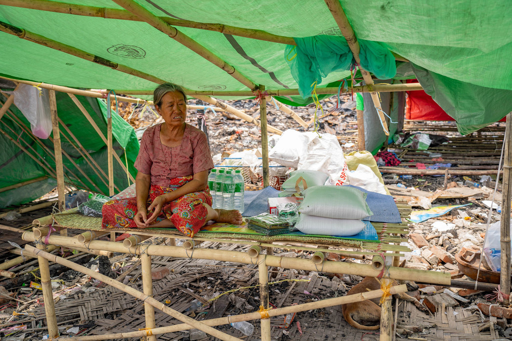 A woman who was affected by the earthquake in Myanmar sits alongside aid items.