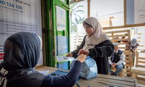 A WFP worker hands a bag of high-energy biscuits to a Palestinian woman in Deir al-Balah, Gaza. The biscuits were donated by the Government of Indonesia. Logos for WFP and Anera are visible in the background.