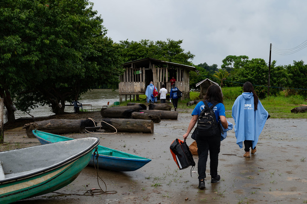 Trabajadores humanitarios de la ONU y la OPS, ataviados con ponchos para la lluvia, caminan hacia una casa de madera sobre pilotes en el Litoral del San Juan, Colombia, como parte de un proyecto de respuesta de emergencia del CERF.