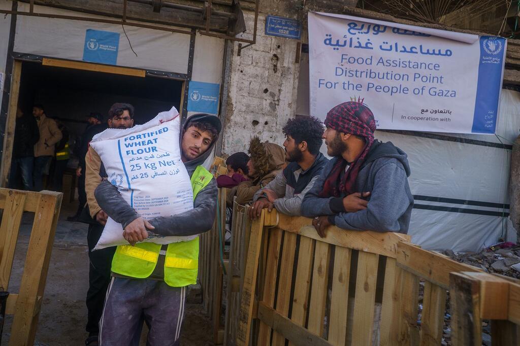 رجل يحمل كيساً من دقيق القمح المدعم بالفيتامينات في نقطة لتوزيع المساعدات الغذائية التابعة لبرنامج الأغذية العالمي في بيت لاهيا، شمال قطاع غزة.