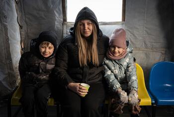 A mother and her two children sit together inside a tent at a heating point in Boryspil, Ukraine, on January 14, 2026. They are warming up and charging devices, as their home lacks electricity for hours. The image highlights the humanitarian crisis affecting displaced families.