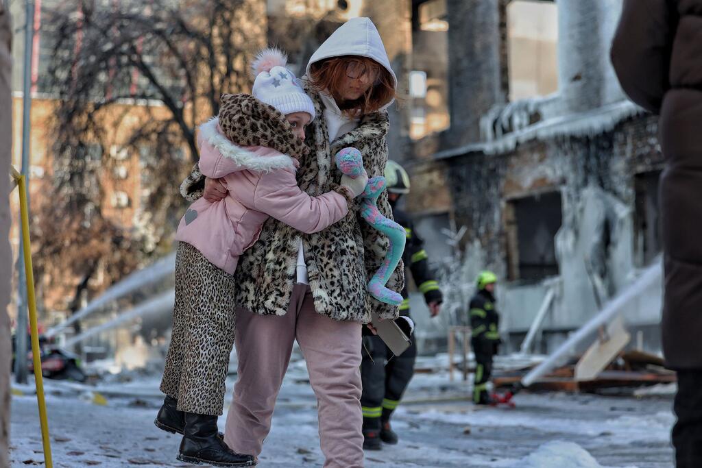 一名母亲带着女儿走过基辅一栋在夜间袭击中严重受损的工业建筑，消防员仍在向这栋建筑的残骸喷水。