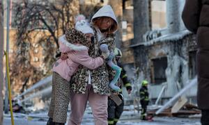A mother and her daughter walk past a heavily damaged industrial building in Kyiv following an overnight attack, as firefighters continue to spray water at the remains.