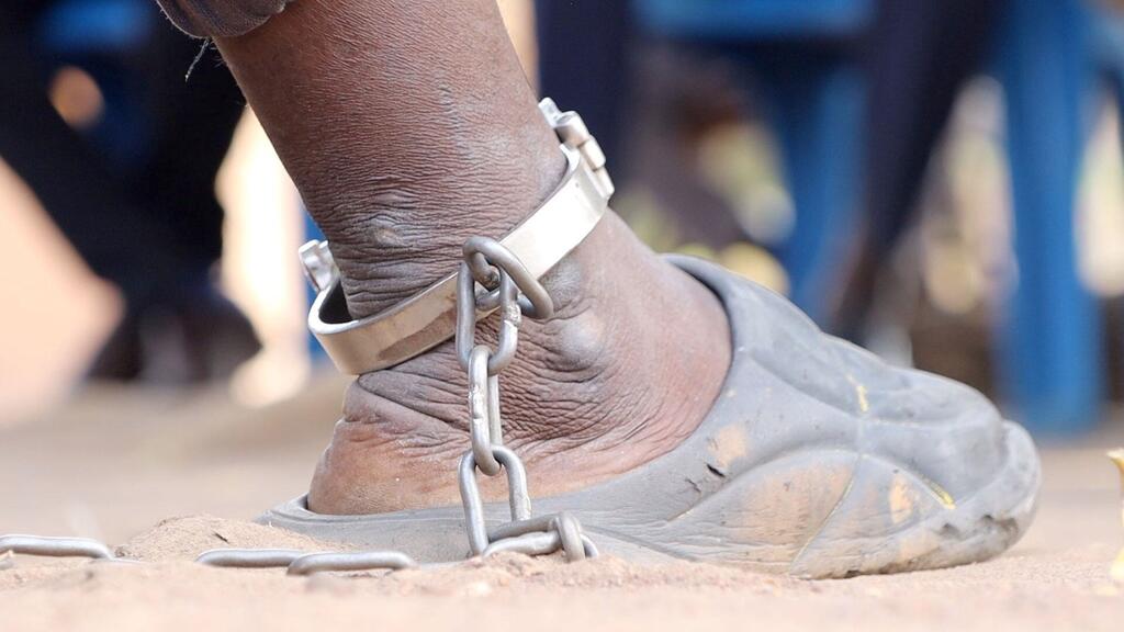 Primer plano del tobillo de un detenido con una cadena metálica y esposas.