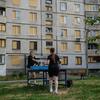 Два человека играют в настольный теннис перед разрушенным войной многоквартирным зданием в Украине с закрытыми окнами.