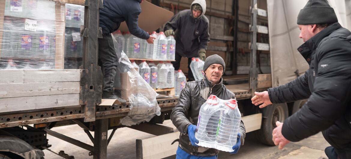 Мужчины выгружают большие бутылки питьевой воды из грузовика в рамках помощи ЮНИСЕФ в Роздилне, Украина, после сильных наводнений, которые загрязнили местные источники воды.