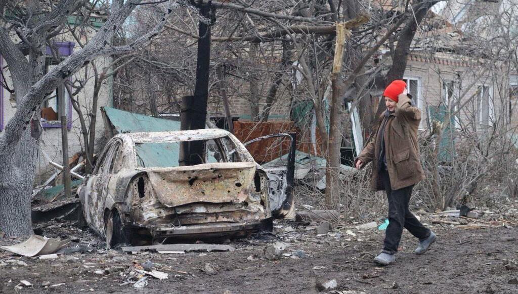 Una mujer con un sombrero rojo pasa junto a un coche calcinado y unos edificios destruidos en Kramatorsk, Ucrania, tras un ataque.