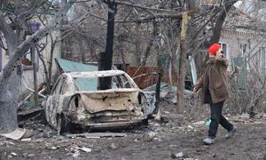 A woman in a red hat walks past a burnt-out car and destroyed buildings in Kramatorsk, Ukraine, following an attack.