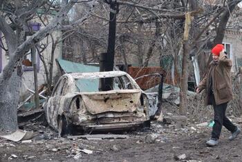 A woman in a red hat walks past a burnt-out car and destroyed buildings in Kramatorsk, Ukraine, following an attack.