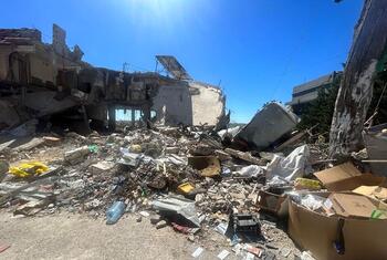 A wide shot of a destroyed building and rubble in Lebanon under a bright blue sky, showing the aftermath of conflict.