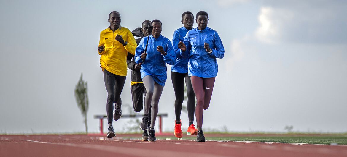 Um grupo de jovens atletas africanos, homens e mulheres, correndo em uma pista vermelha durante uma sessão de treinamento no Centro Nacional de Treinamento de Alta Altitude de Teryet, no distrito de Kapchorwa, Uganda.