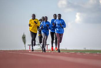 Un groupe de jeunes athlètes africains, hommes et femmes, en train de courir sur une piste rouge lors d'une séance d'entraînement au centre national d'entraînement en haute altitude de Teryet, dans le district de Kapchorwa, en Ouganda.