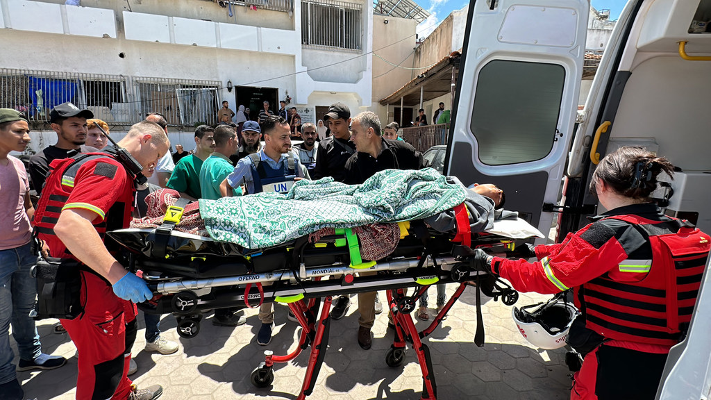 Wahudumu wa afya waliovalia fulana nyekundu na glavu za bluu wanampakia mgonjwa kwenye machela kwenye gari la wagonjwa katika Hospitali ya Al-Ahli huko Gaza.