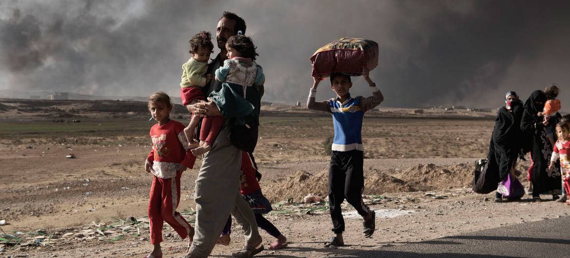A newly displaced man carries two children at a check point in Qayyara, south of Mosul, Iraq. (file)