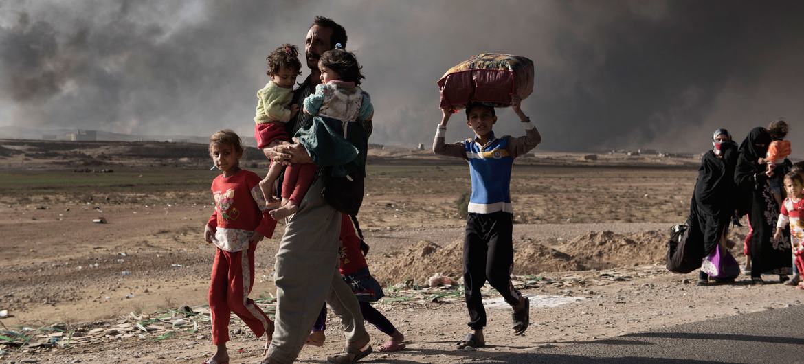 Un homme déplacé porte dans ses bras deux enfants vers un point de contrôle à Qayyara, au sud de Mossoul, en Iraq (photo d'archives).