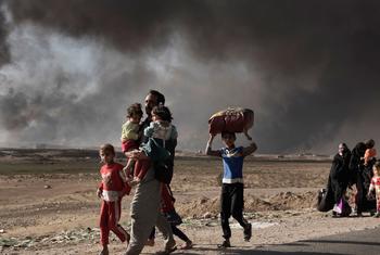 Um homem recentemente deslocado carrega duas crianças num posto de controle em Qayyara, ao sul de Mosul, no Iraque (arquivo)