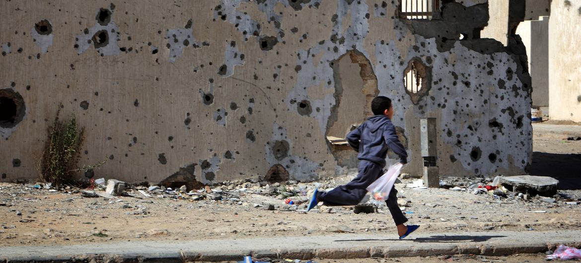 A boy runs past damaged buildings, defaced by shelling during the conflict, on his way home from shopping, in the city of Sirte.