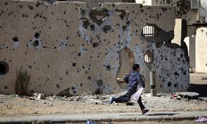 A boy runs past damaged buildings, defaced by shelling during the conflict, on his way home from shopping, in the city of Sirte.