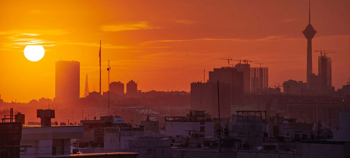 A stunning sunset view of Tehran, Iran's capital city, showcasing its skyline with iconic buildings and the Milad Tower silhouetted against an orange sky.