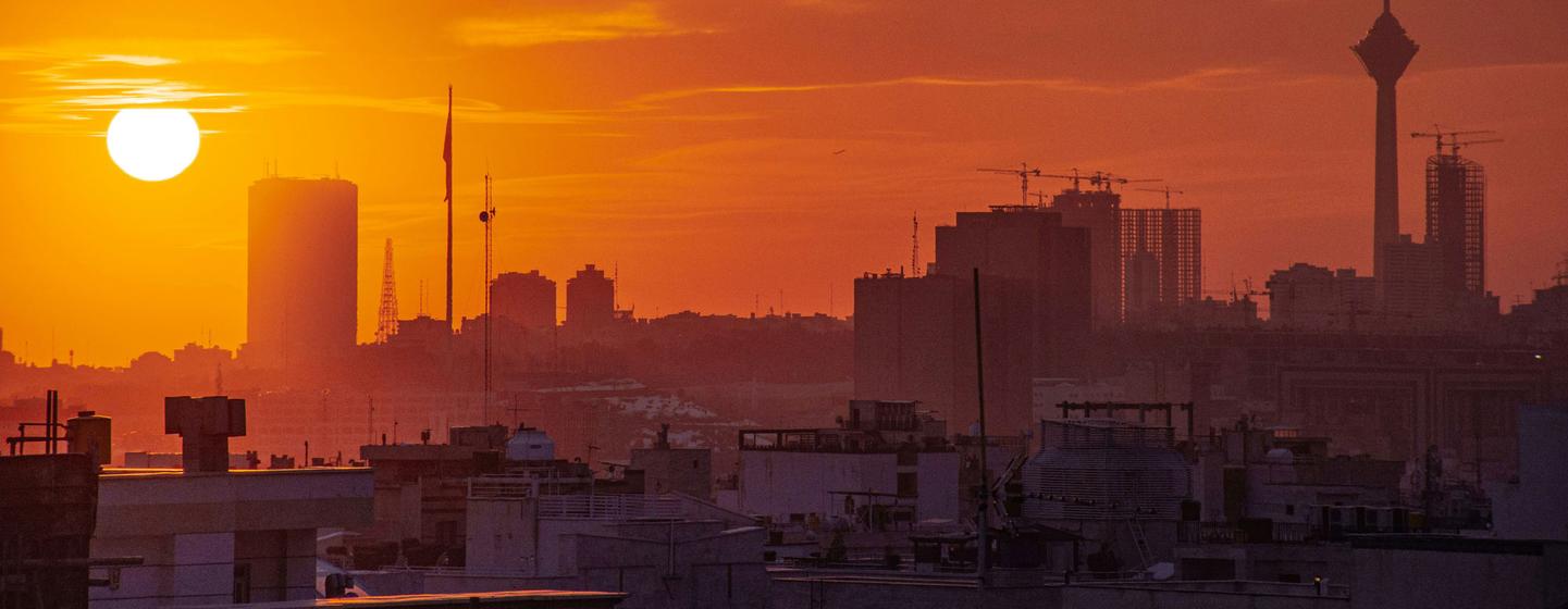 Une vue époustouflante du coucher du soleil sur Téhéran, la capitale de l'Iran, qui présente son skyline avec des bâtiments emblématiques et la tour Milad en silhouette contre un ciel orange.
