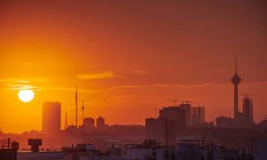 A stunning sunset view of Tehran, Iran's capital city, showcasing its skyline with iconic buildings and the Milad Tower silhouetted against an orange sky.