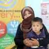 Uma parteira no Afeganistão segura uma criança pequena enquanto está em frente a um cartaz de uma campanha de saúde do Unfpa .