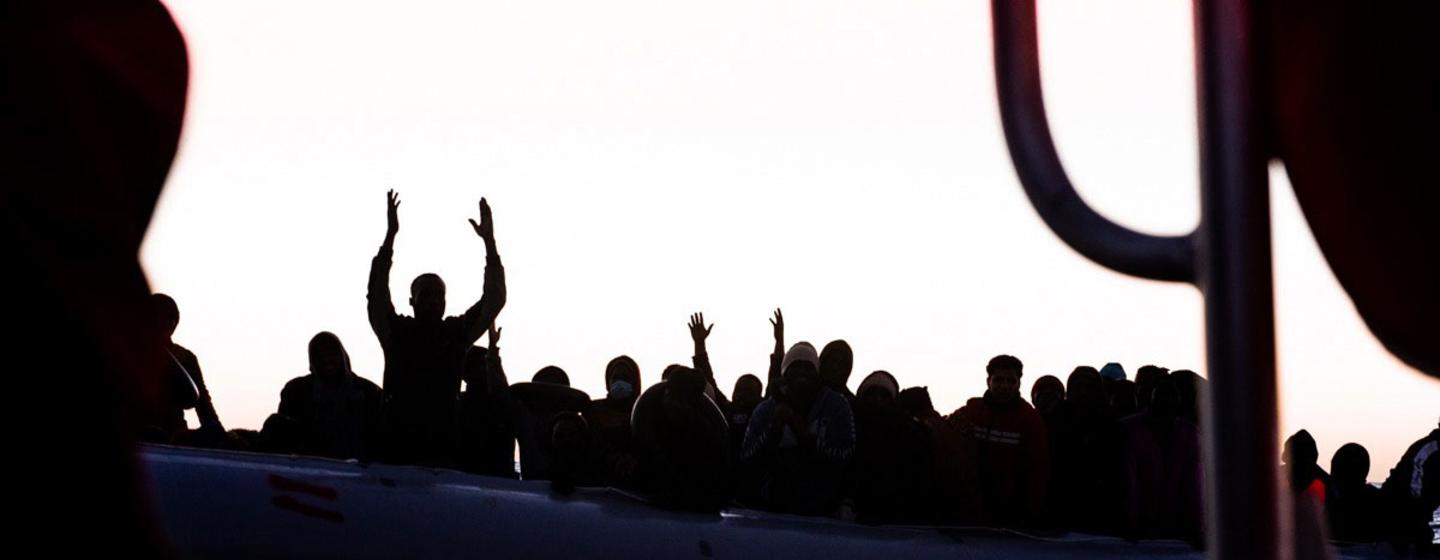 Des silhouettes de migrants et de réfugiés sur un radeau gonflable surpeuplé lèvent les mains lors d'une opération de sauvetage par l'Ocean Viking en mer Méditerranée.