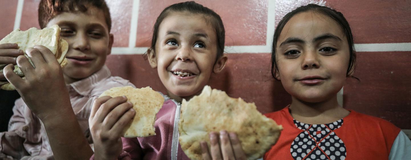 Children sheltering at an UNRWA school in Gaza enjoy bread distributed by WFP.