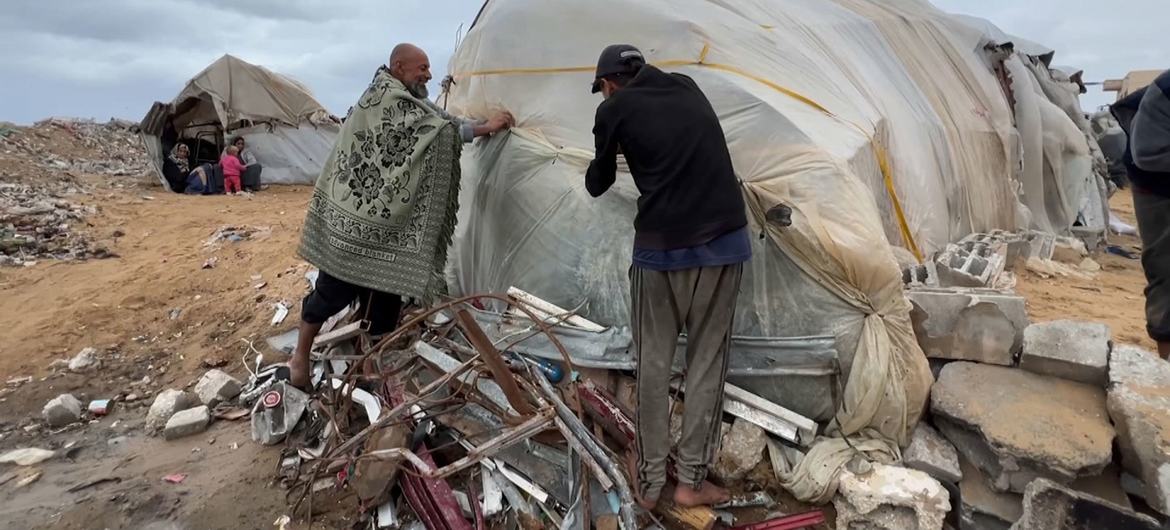Dois homens protegem a lateral de um abrigo enquanto o inverno continua em Gaza Dois homens protegem a lateral de um abrigo enquanto o inverno continua em Gaza
