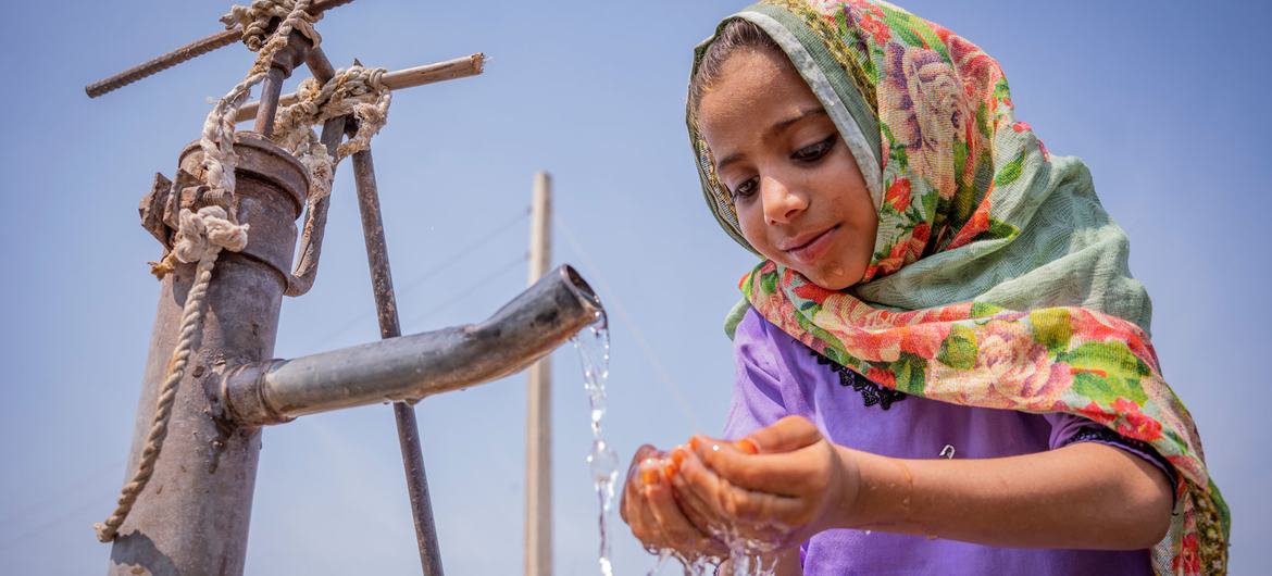 Uma menina de seis anos bebe água de uma bomba manual comunitária no Paquistão.