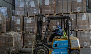 Hala, mwanamke Mpalestina, anaendesha forklift ya rangi ya manjano ya WFP ndani ya ghala lililojaa misaada ya kibinadamu huko Gaza.