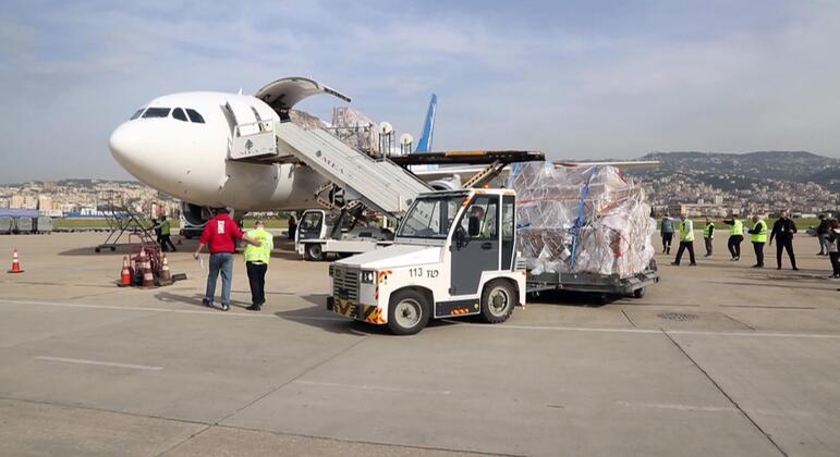 Fornecimentos médicos sendo descarregados de um avião no Aeroporto Internacional Rafik Hariri no Líbano, com trabalhadores e veículos do aeroporto visíveis.