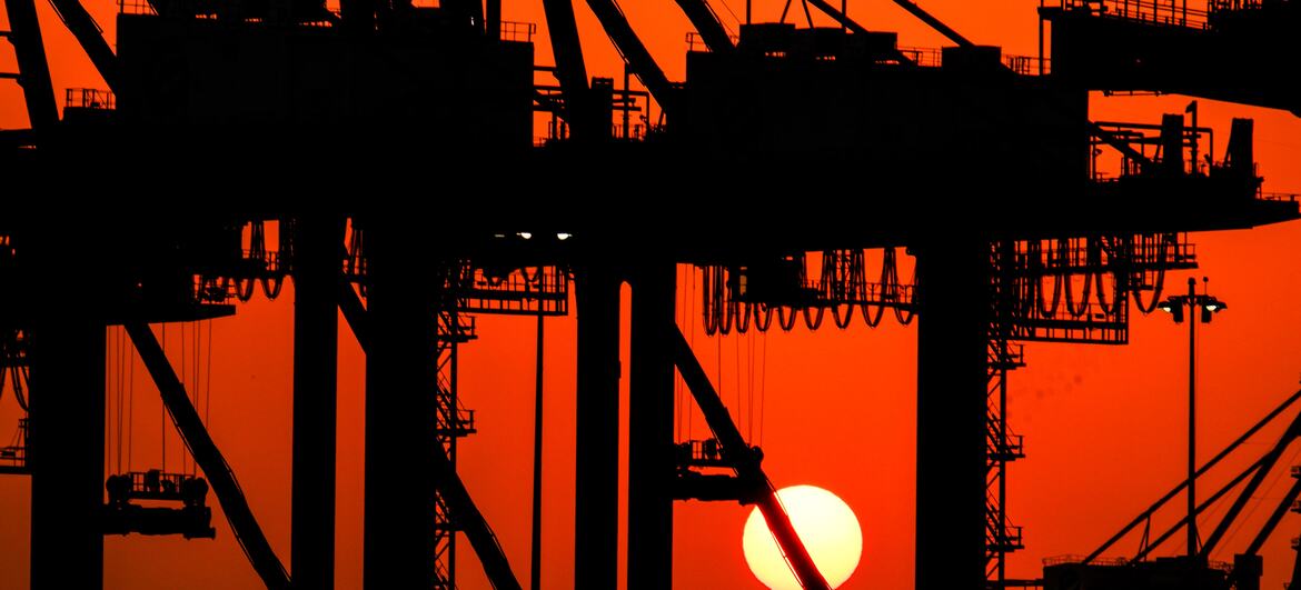Silhouette of large cargo cranes at a container terminal against a vibrant orange sunset sky.