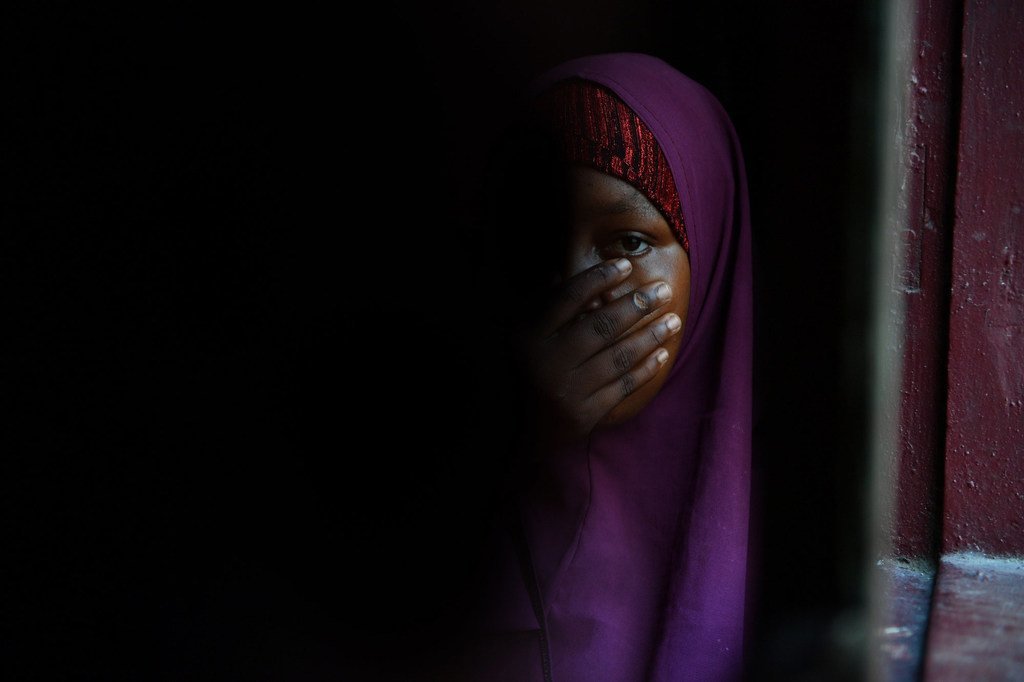 Mwanamke wa Kisomali aliyevaa hijabu ya zambarau anafunika mdomo wake kwa mkono wake, uso wake ukifichwa na kivuli.